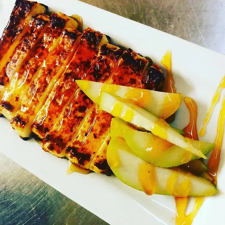 A white plate topped with a piece of meat and sliced apples