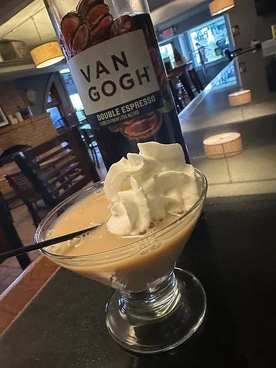 A martini with whipped cream and a bottle of van gogh in the background