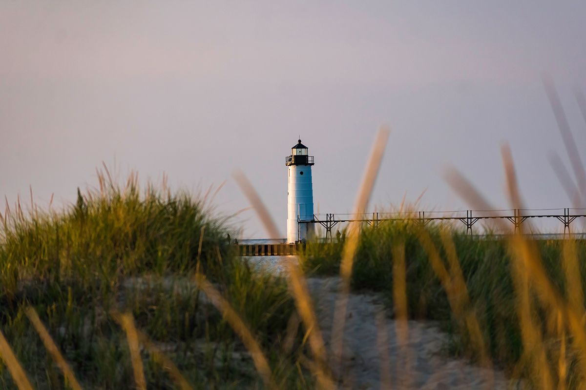 A lighthouse is visible through the tall grass on the beach.