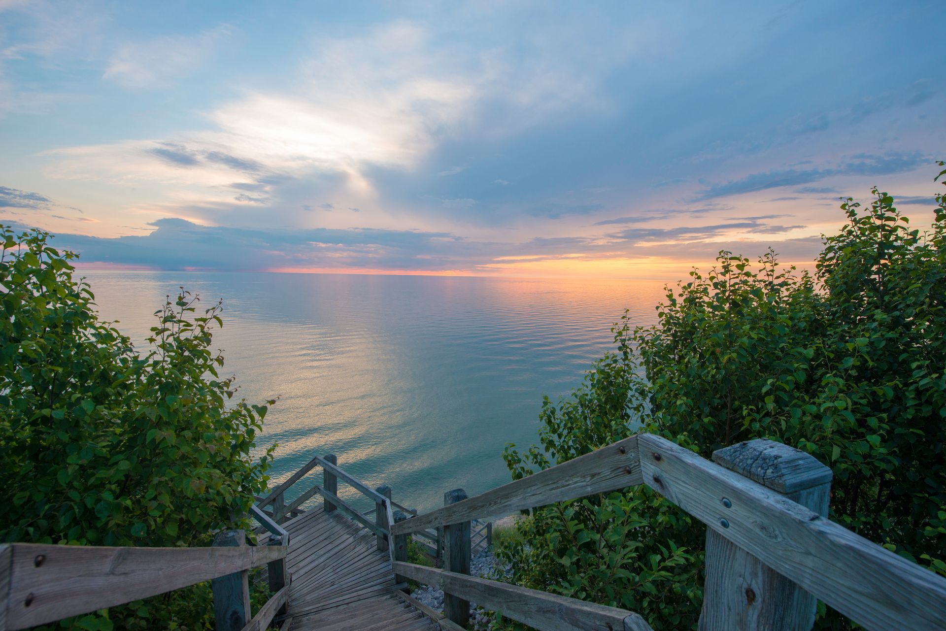 A wooden walkway leading to the ocean at sunset.