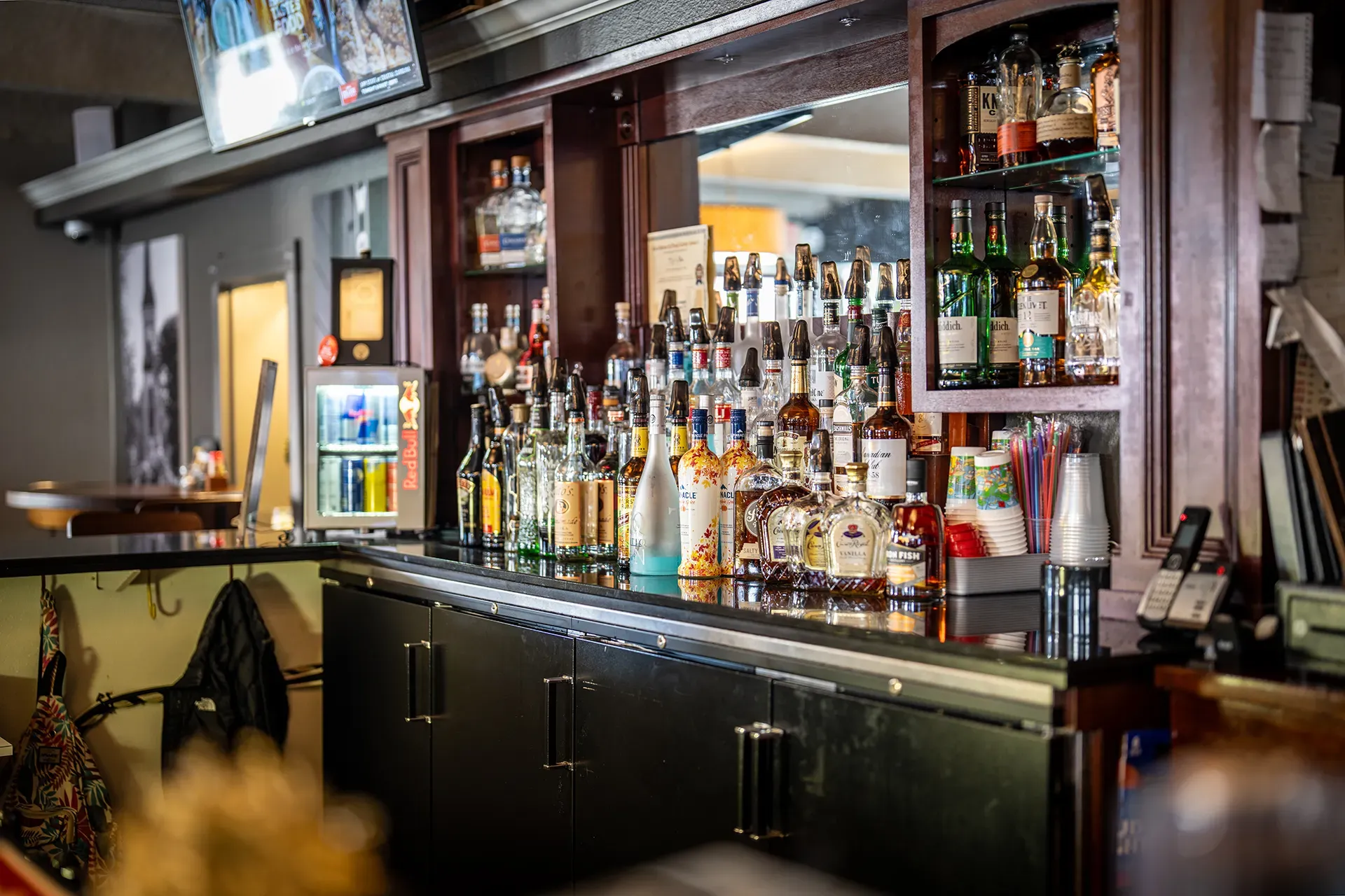 A bar filled with lots of bottles of liquor and a refrigerator.
