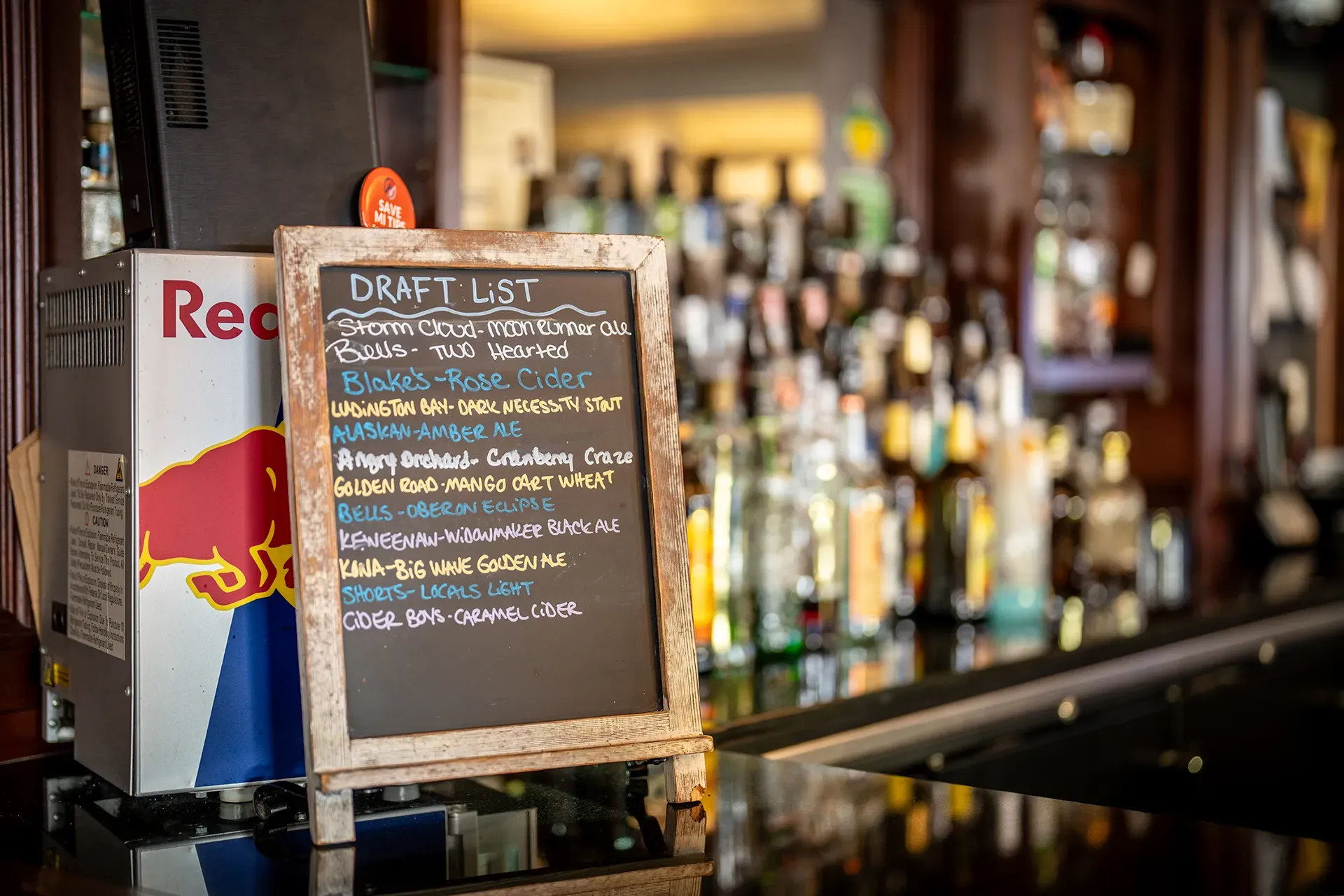 A chalkboard with a drink list on it is sitting on a bar.