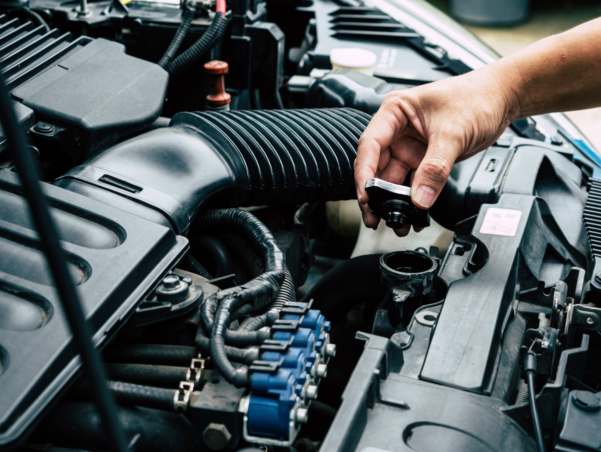 A person's hand opens the radiator cap on a car engine.
