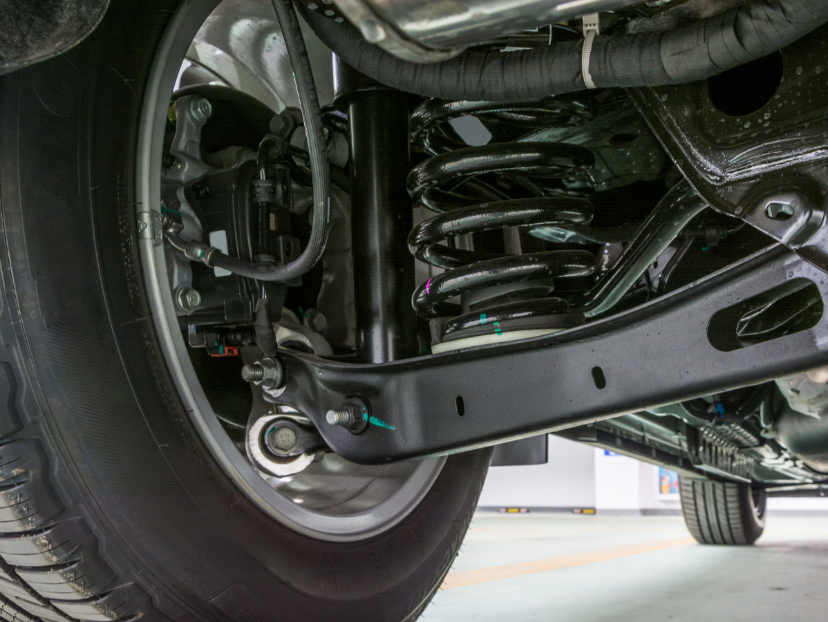 A close-up view of a car’s rear suspension system, featuring a black coil spring, shock absorber, and control arm.