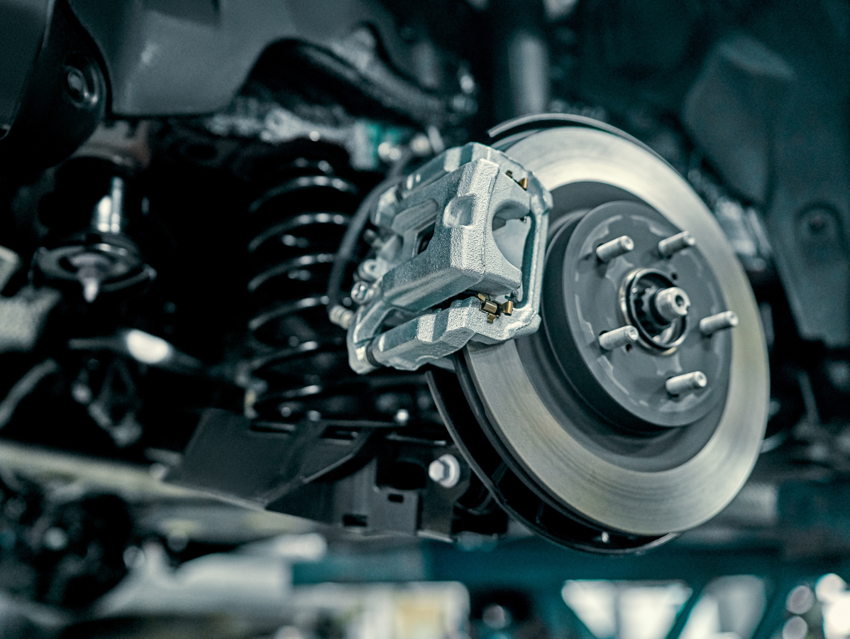 Close-up of a vehicle’s disc brake assembly, brake caliper, and coil spring suspension system.