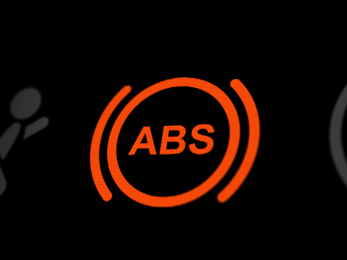 An illuminated orange ABS warning light on a black vehicle dashboard display, indicating an anti-lock brake system issue.
