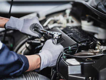 A mechanic wearing gray gloves uses a ratchet wrench to work on a car engine.