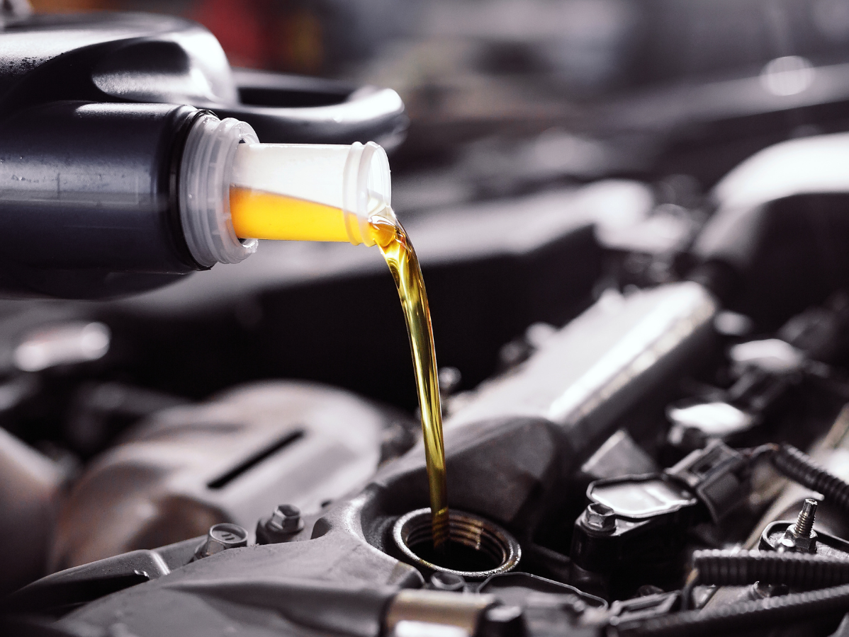 Yellow motor oil being poured from a black plastic bottle into a car engine.