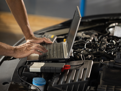 A mechanic uses a laptop and diagnostic device to inspect a car engine in a garage.