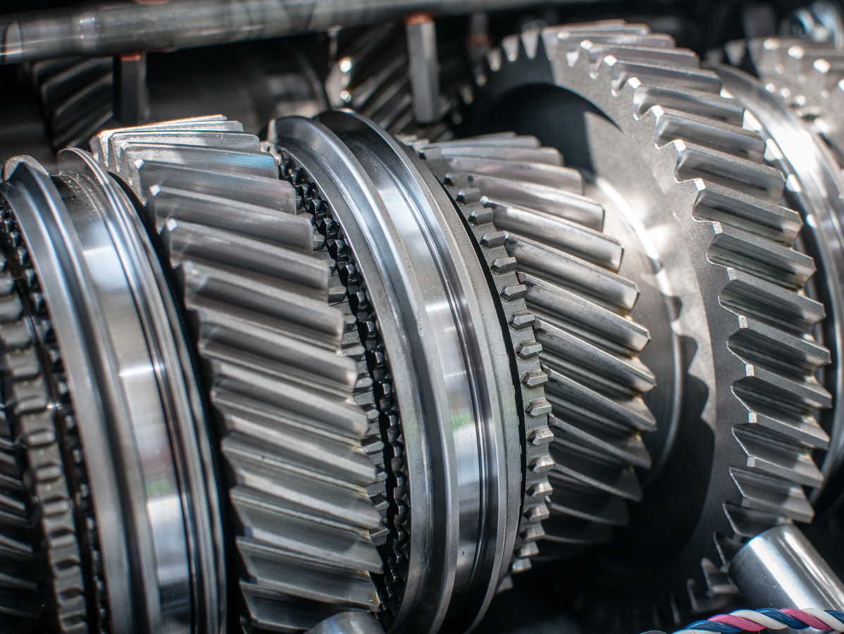 Close-up of polished, metallic helical gears and mechanical components inside a vehicle transmission system.