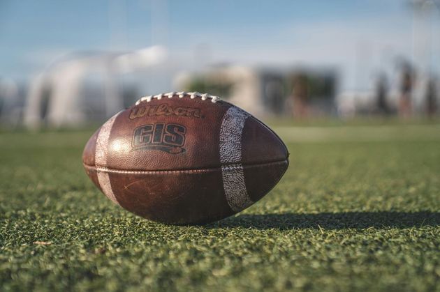 Football player in silver uniform runs with ball on a green field.
