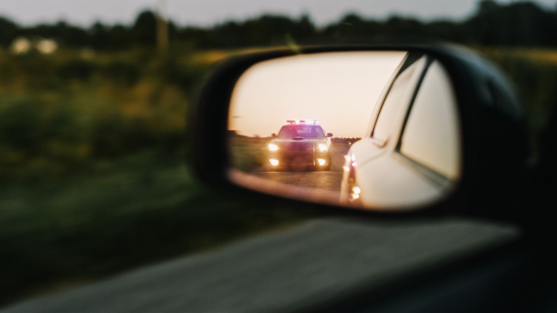 A police car is reflected in the rear view mirror of a car.