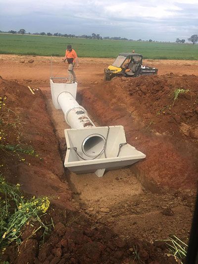 A man is standing next to a large pipe in a trench.