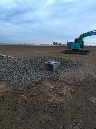 A blue excavator is sitting on top of a pile of gravel in a dirt field.