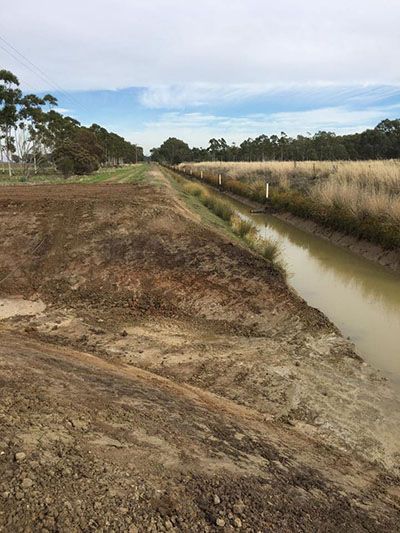 A river runs through a dirt field next to a dirt road.