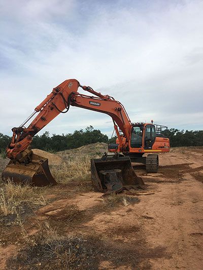 A large orange excavator is sitting on top of a dirt field.