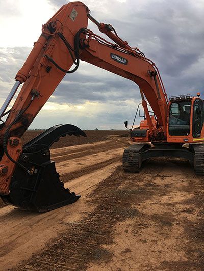 A large orange excavator is sitting on top of a dirt road.