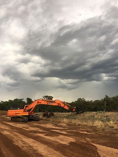 A large orange excavator is sitting in a dirt field under a cloudy sky.