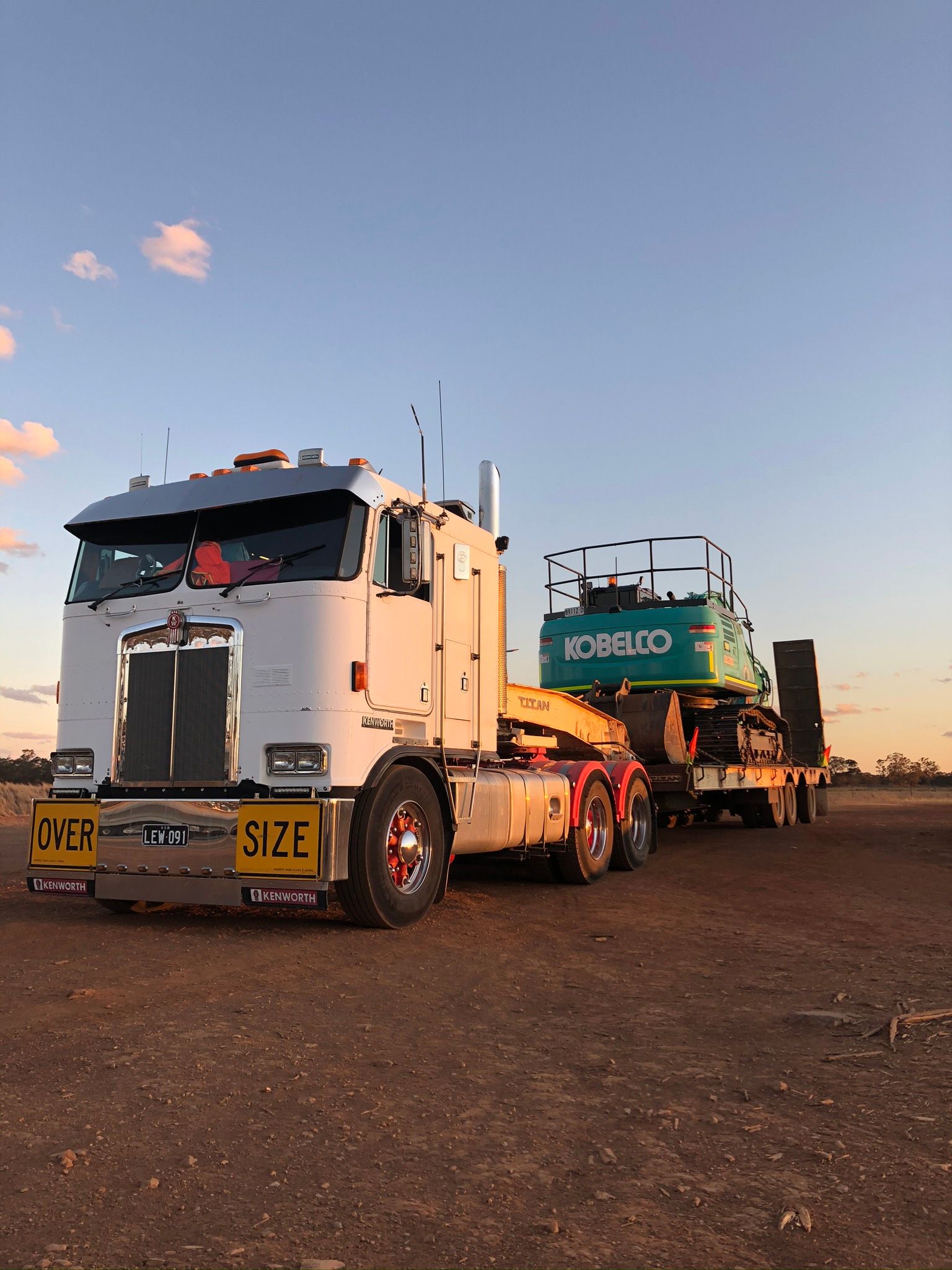A white semi truck is carrying a green excavator on a trailer.