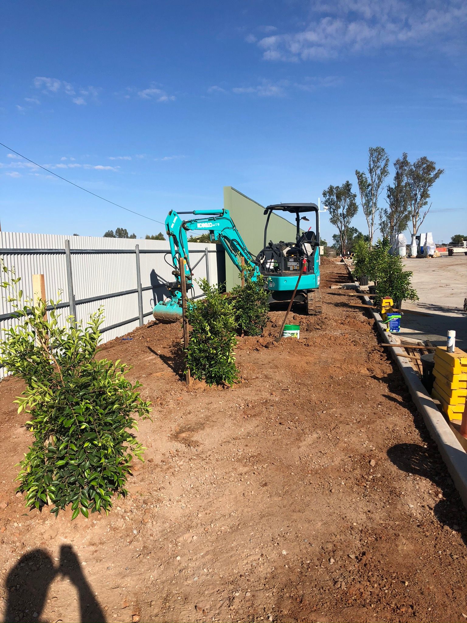 A small excavator is sitting in the dirt next to a fence.
