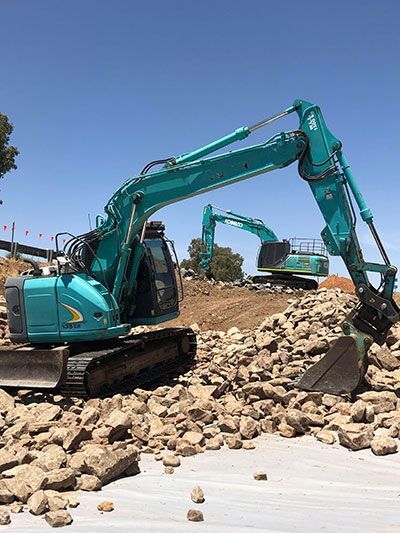 A green excavator is sitting on top of a pile of rocks.