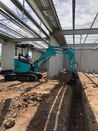 A blue excavator is digging a hole in the dirt in a building under construction.