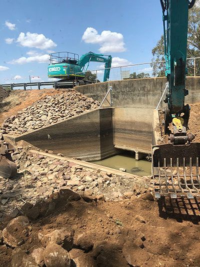 An excavator is digging a hole in the ground next to a pile of rocks.