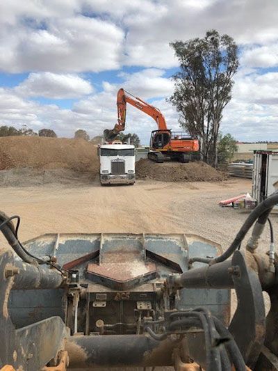 A bulldozer is loading dirt into a truck in a dirt field.