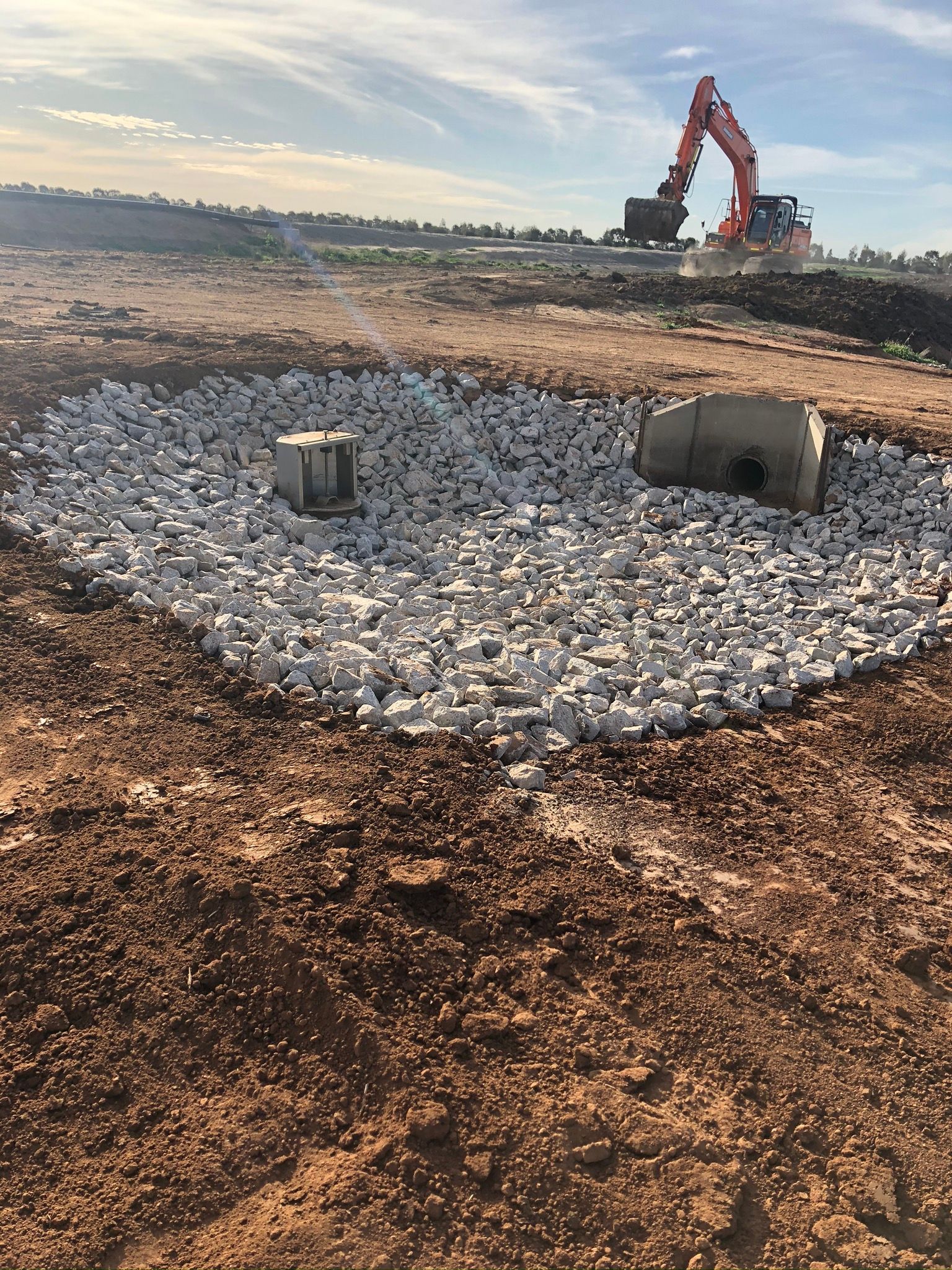 A large excavator is sitting on top of a pile of gravel in a dirt field.