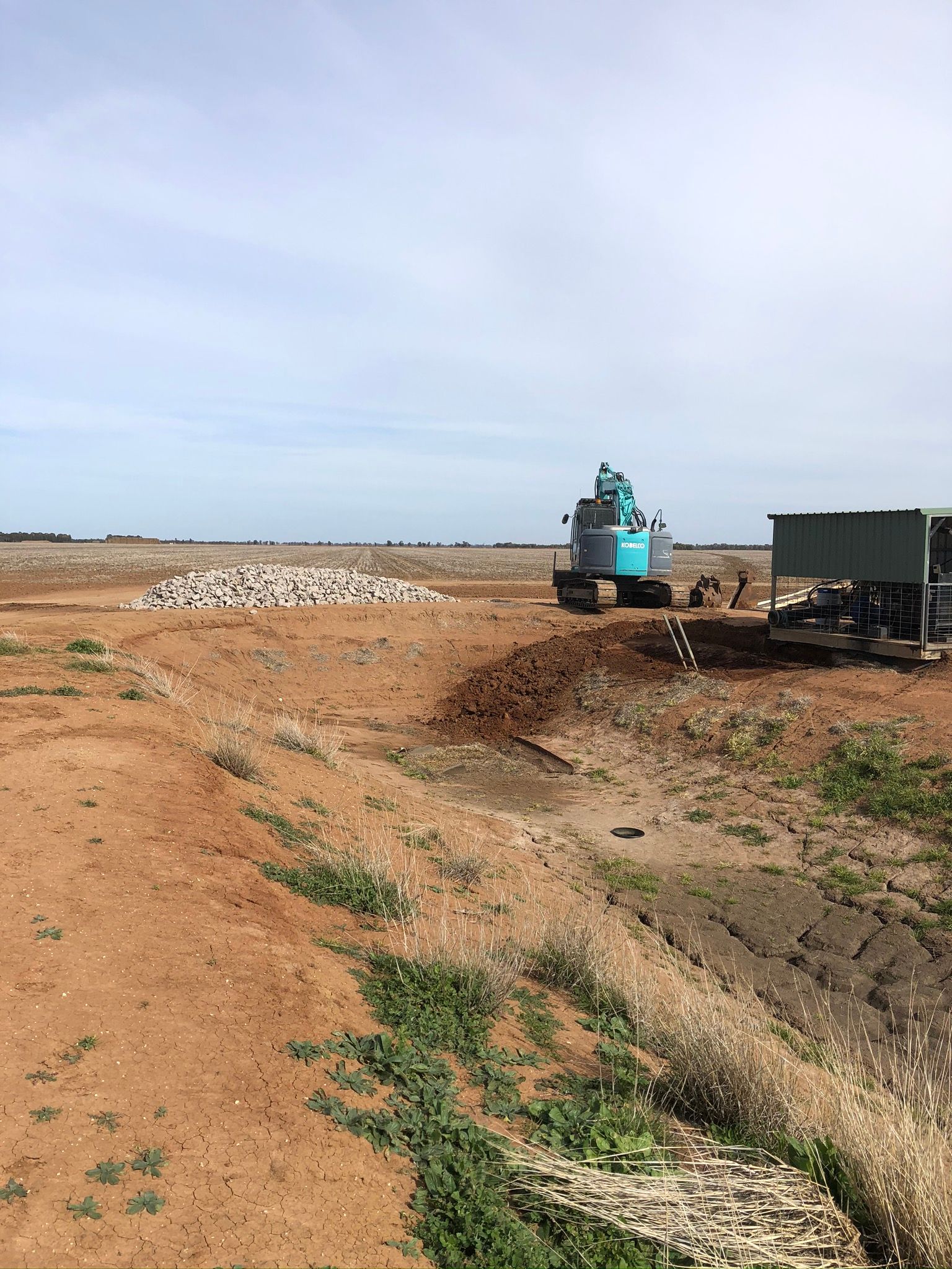 A blue excavator is working on a dirt field.