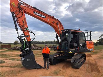 A man is standing in front of a large orange excavator.