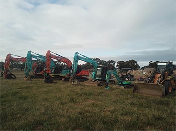 A row of construction vehicles are parked in a grassy field.