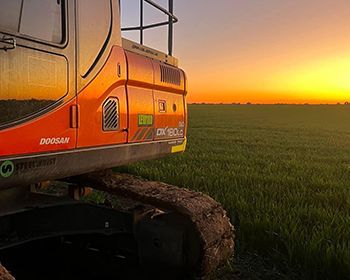 A bulldozer is parked in a grassy field at sunset.