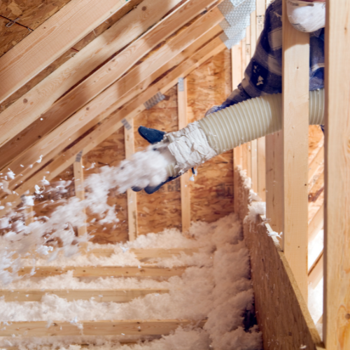 A person is blowing insulation into the attic of a house