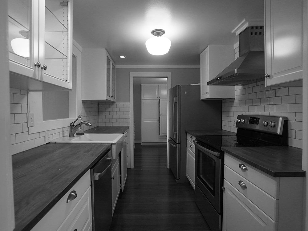 A black and white photo of a kitchen with white cabinets and stainless steel appliances.