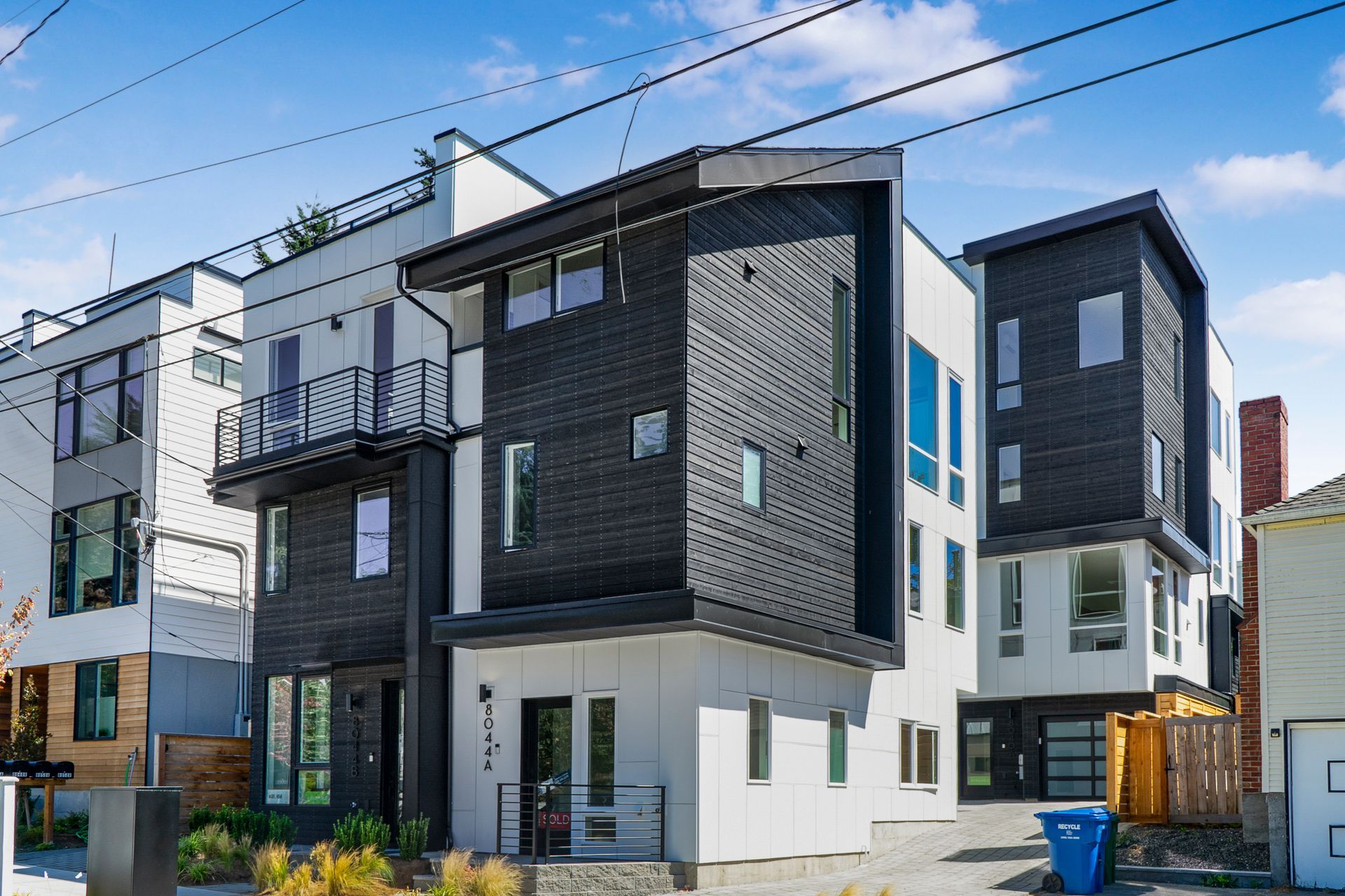 A row of black and white buildings with a blue trash can in front of them.