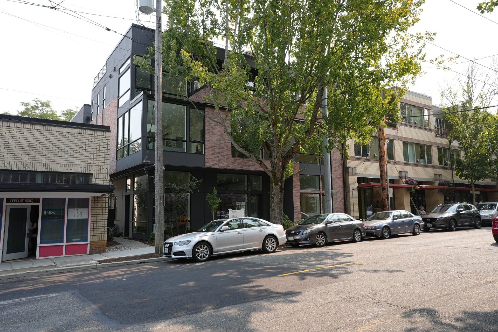 A row of cars are parked on the side of the road in front of a building.