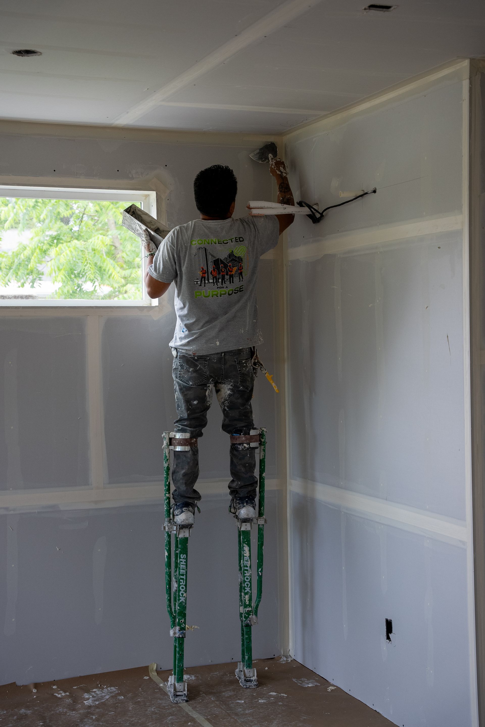 A man is standing on stilts and plastering a wall.