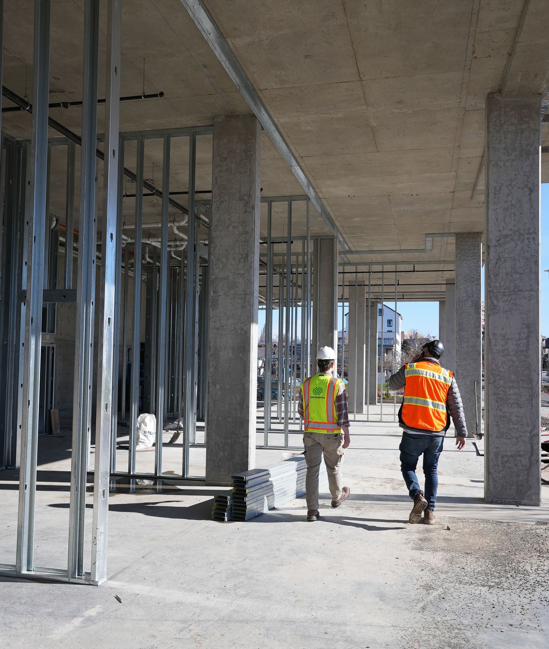 Two construction workers are walking through a building under construction