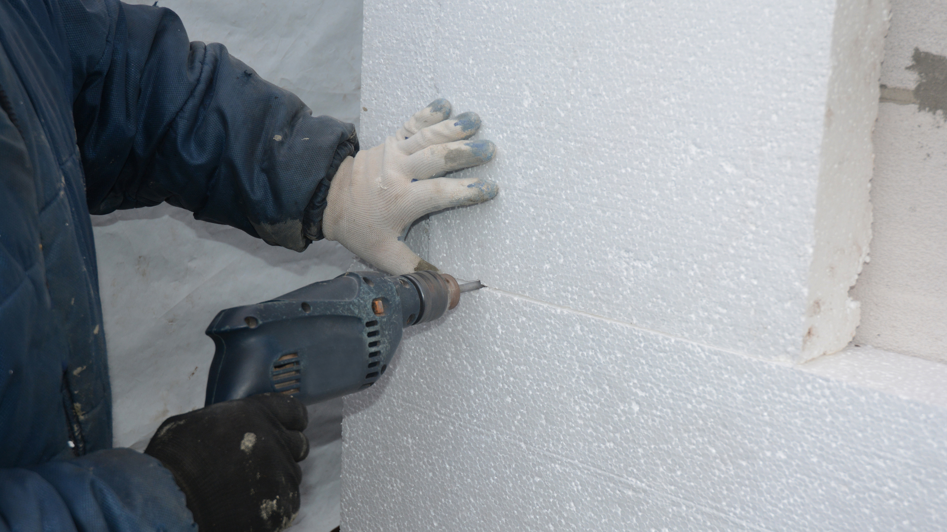 A man is using a drill to drill a hole in a piece of styrofoam.