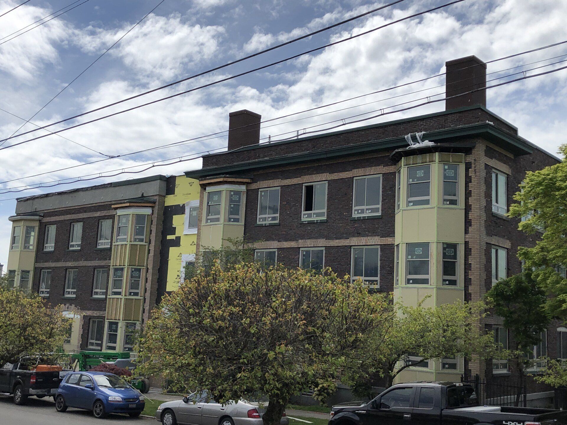 A large brick building under construction with cars parked in front of it.