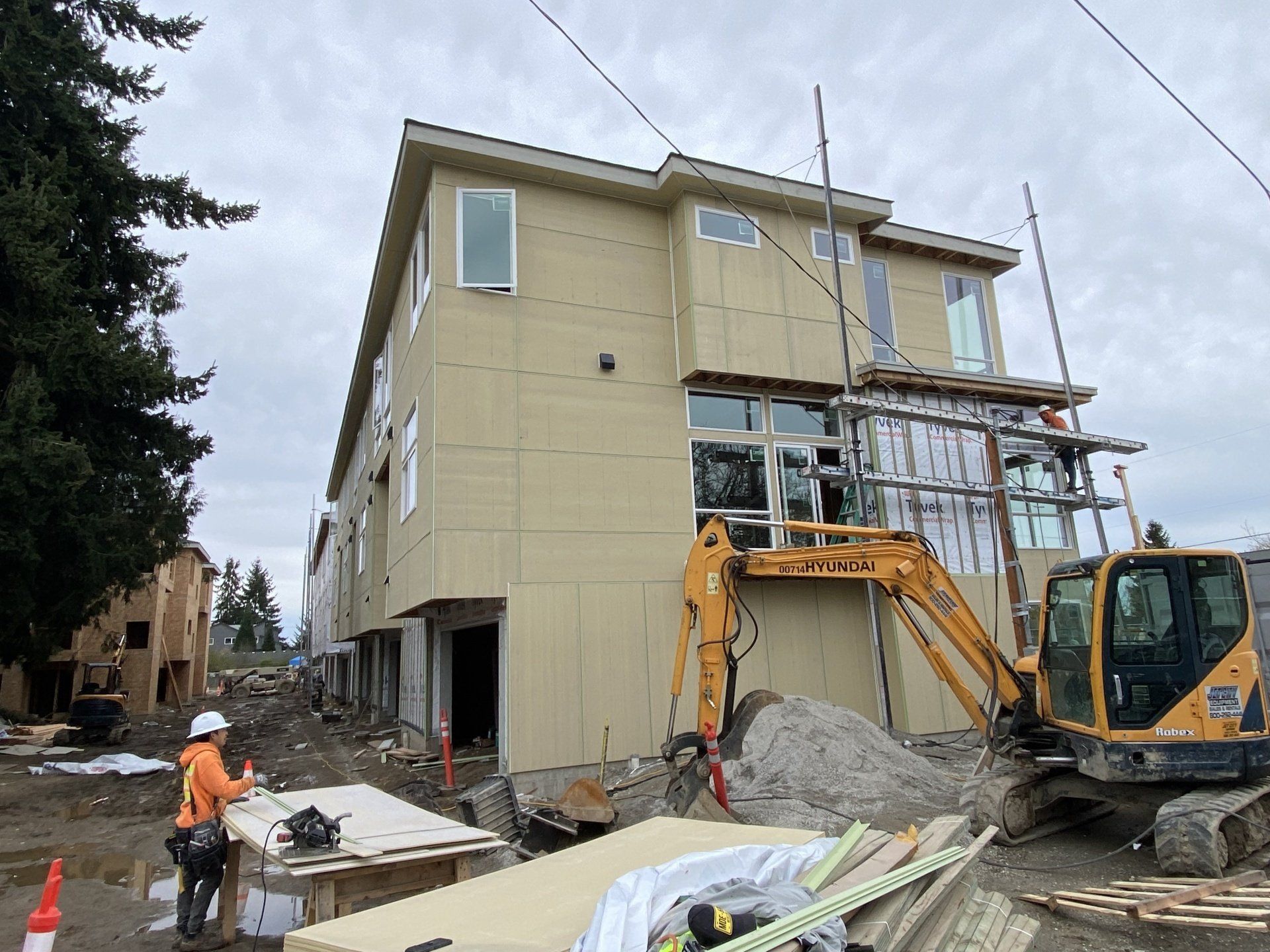 A large house is being built with a yellow excavator in front of it.