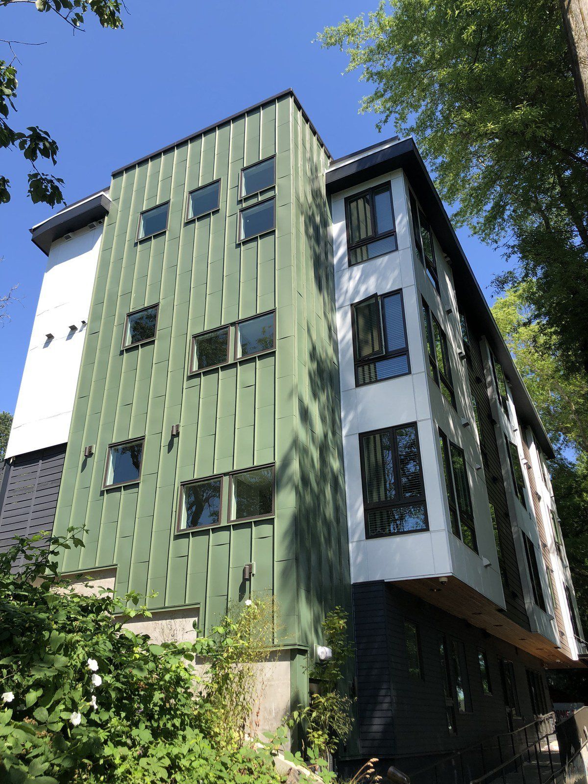 A large green and white building with lots of windows is surrounded by trees.