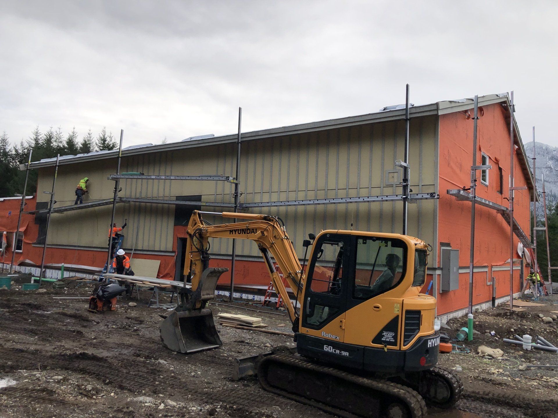 A yellow excavator is parked in front of a building under construction.