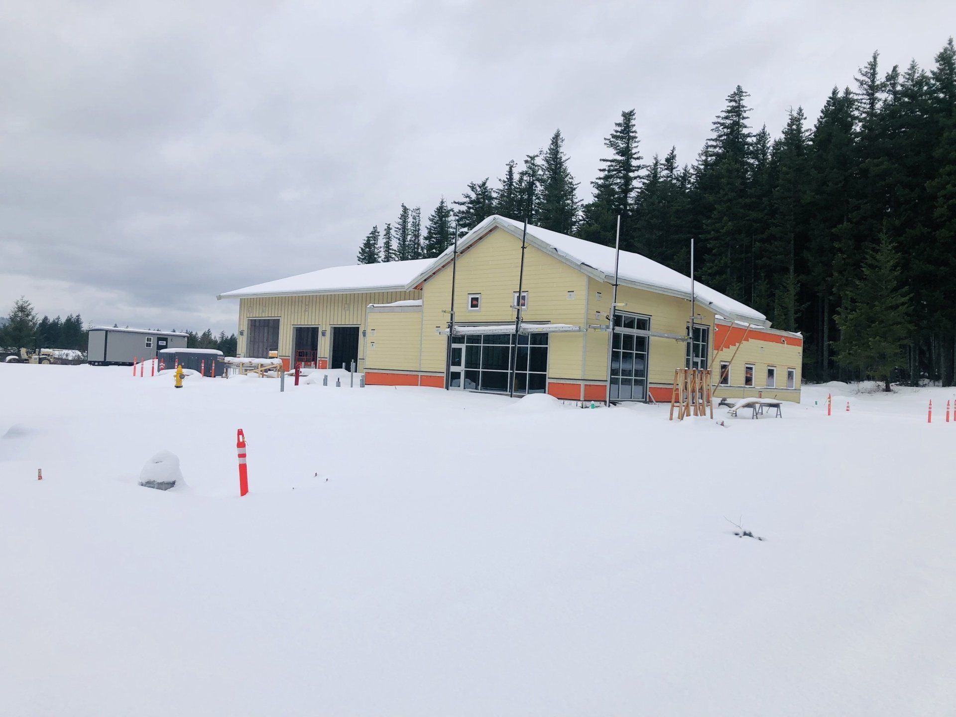 A building under construction is surrounded by snow and trees.