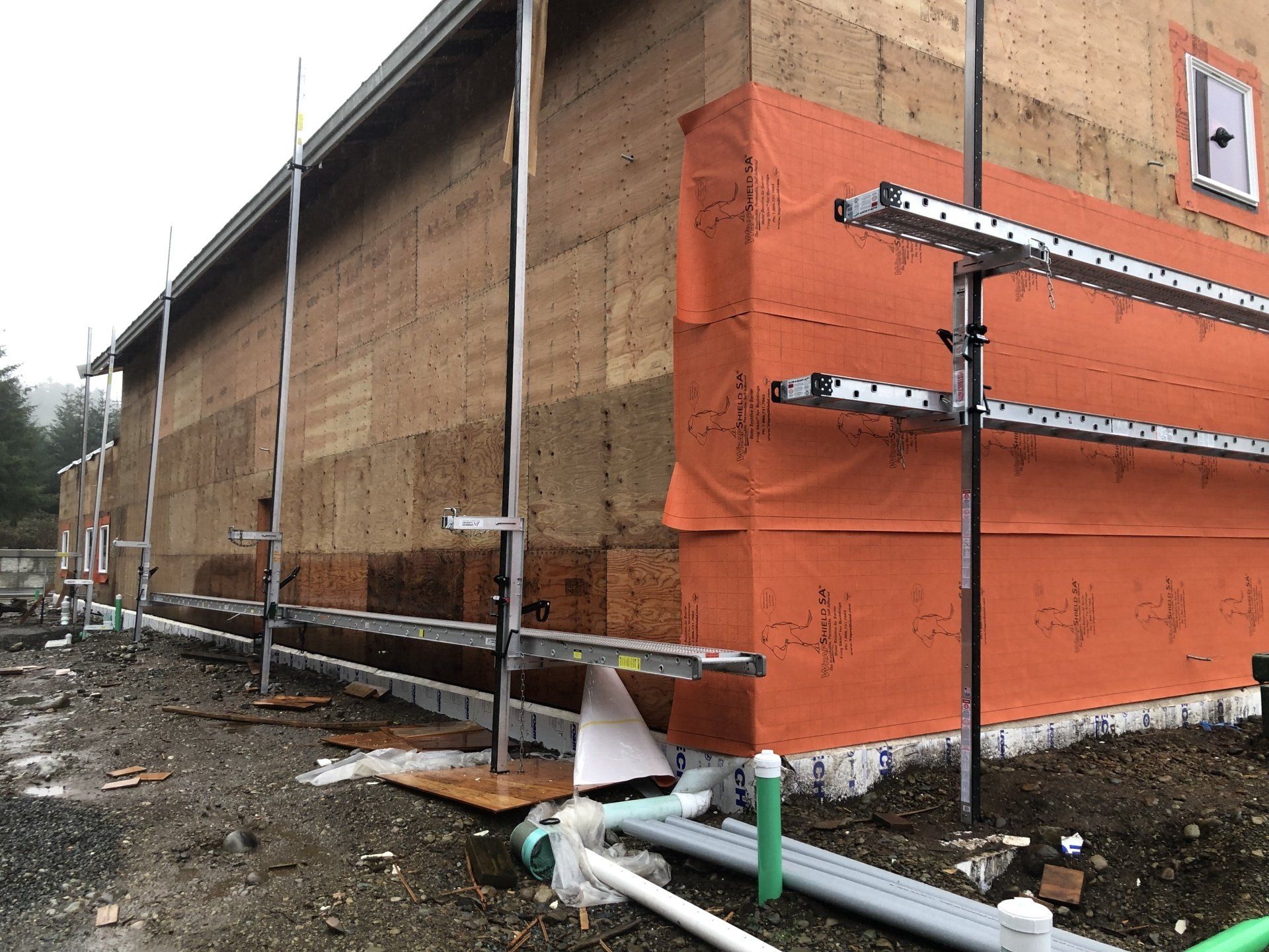 The side of a building is covered in orange tarps and pipes.