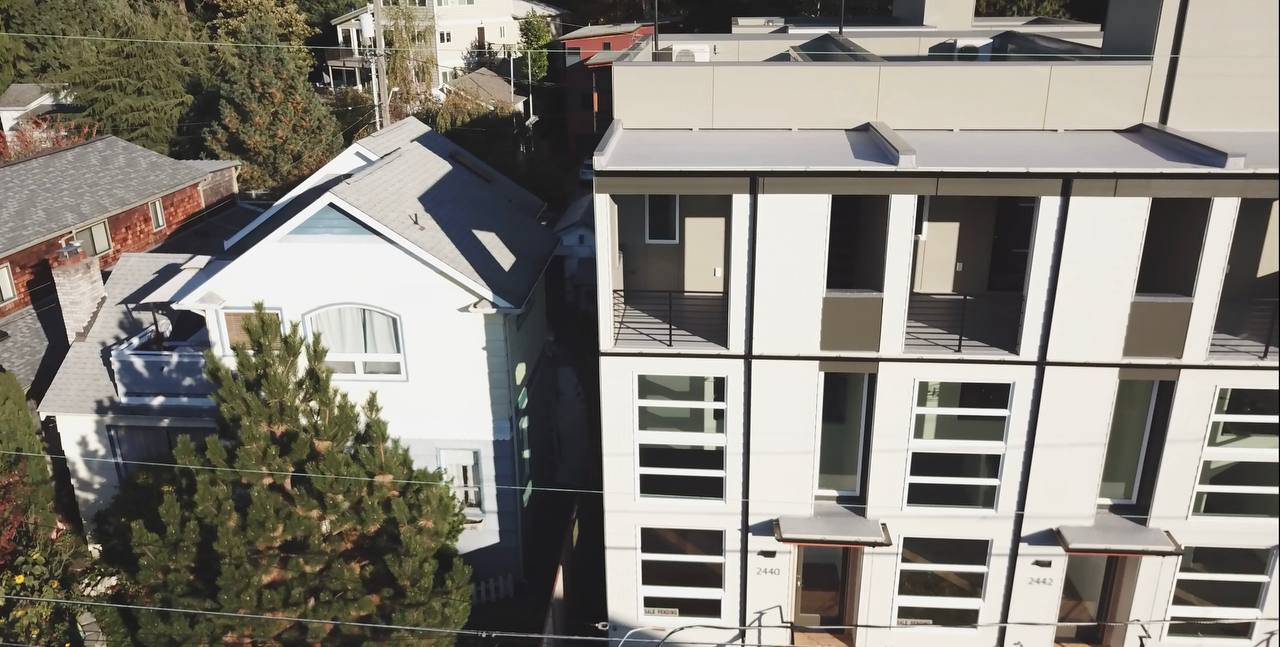 An aerial view of a building with a lot of windows and a house in the background.