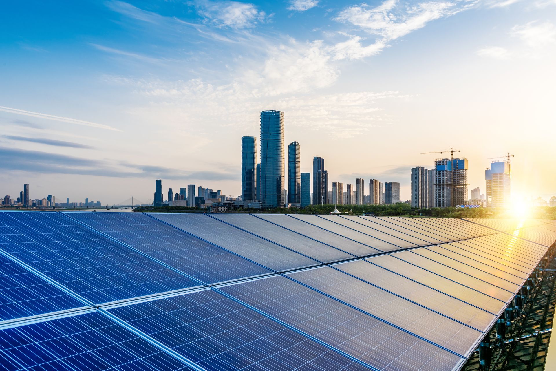 A row of solar panels on top of a building with a city skyline in the background.