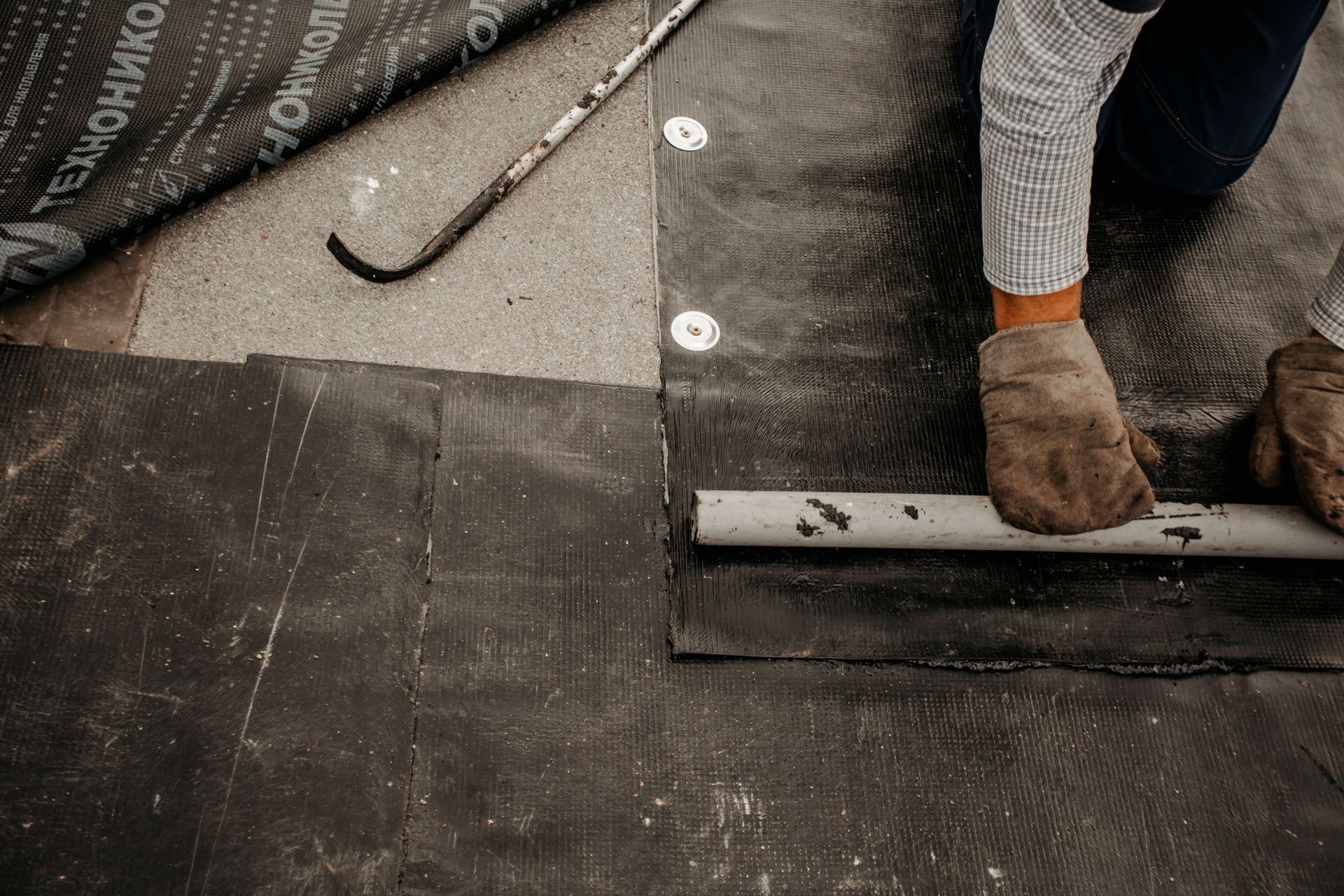 Close-up of a roofer installing a waterproof membrane during commercial flat roof construction. Close-up of a roofer installing a waterproof membrane during commercial flat roof construction.