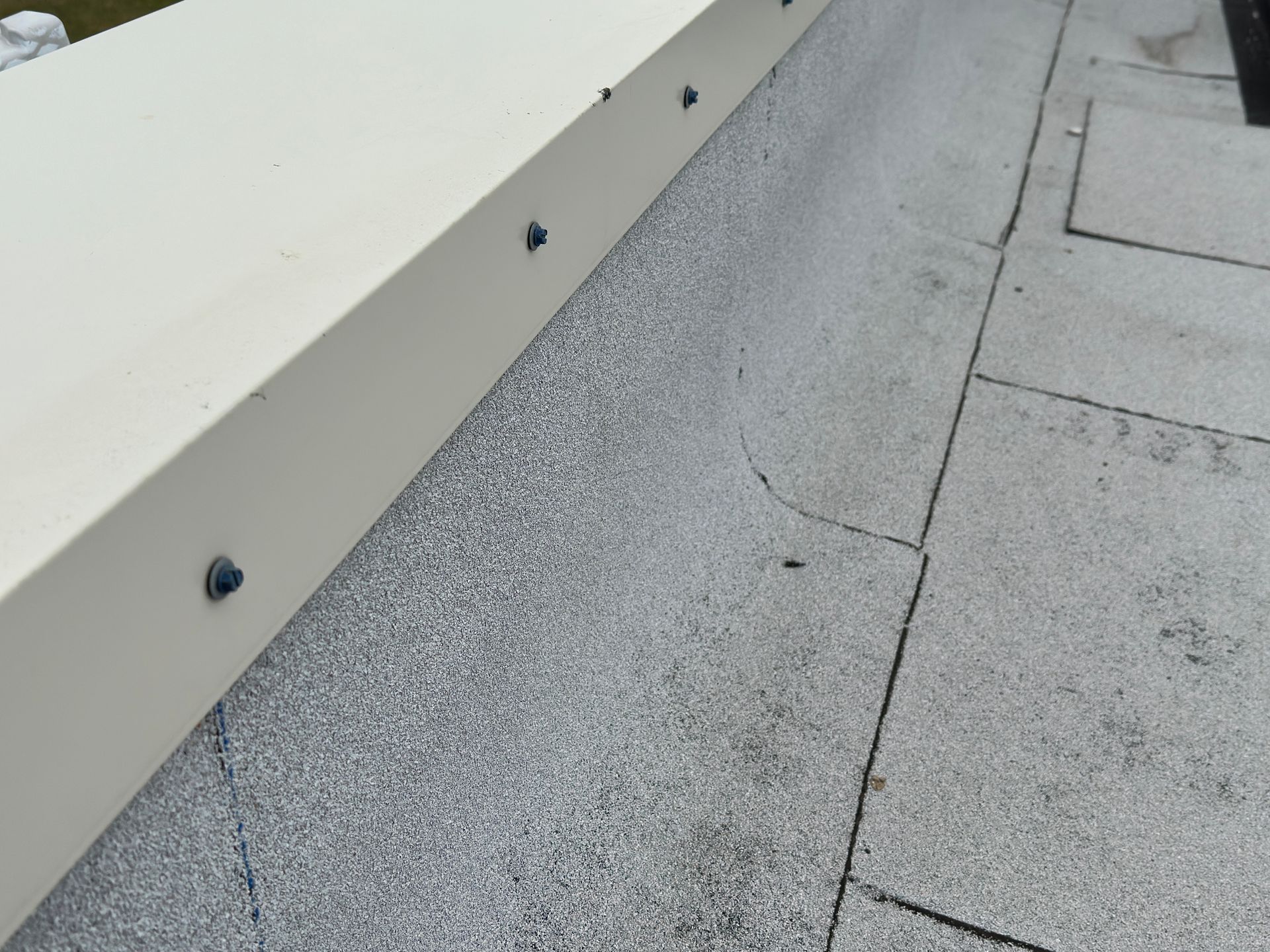 Flat roof with grey textured material and white metal flashing secured along the edge.